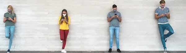 Masked young people using smartphones while socially distancing in line.